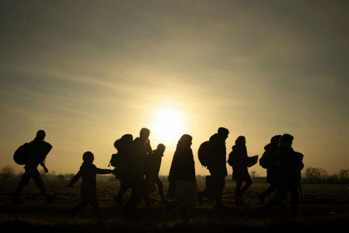 Silhouetted group of refugees walking towards the sunset
