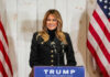 First Lady BREAKS Silence—Exposes Elite Network A woman in a black jacket smiling at a podium with a Trump sign and American flags in the background