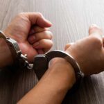 Close-up of hands in handcuffs resting on a wooden surface