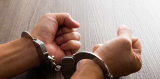 Close-up of hands in handcuffs resting on a wooden surface