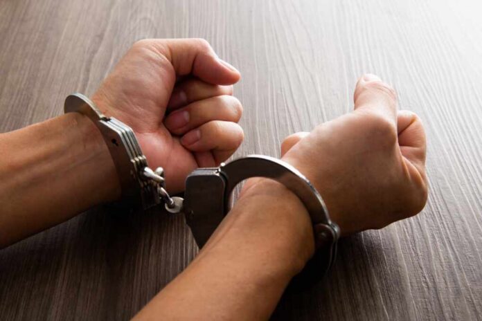 shutterstock_2111823440.jpg Close-up of hands in handcuffs resting on a wooden surface