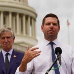 Two men at a press conference outside the Capitol building, one speaking into a microphone