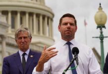 Two men at a press conference outside the Capitol building, one speaking into a microphone