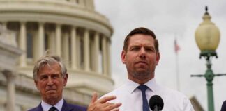 Two men at a press conference outside the Capitol building, one speaking into a microphone