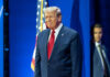 A man in a suit smiling at a political event with an American flag in the background