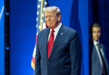 A man in a suit smiling at a political event with an American flag in the background