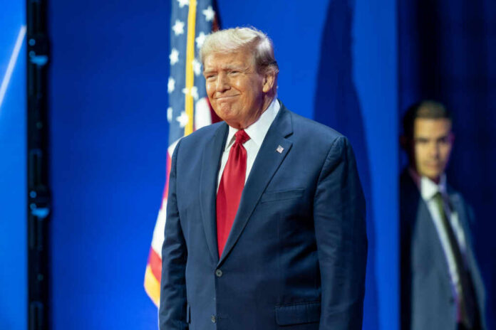 A man in a suit smiling at a political event with an American flag in the background