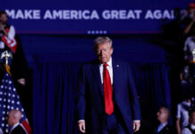 A man in a suit with a red tie walking towards the camera at a political rally