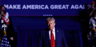 A man in a suit with a red tie walking towards the camera at a political rally