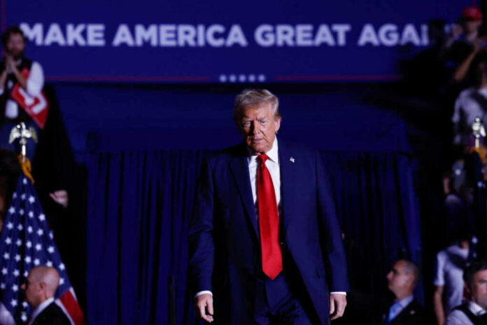 A man in a suit with a red tie walking towards the camera at a political rally
