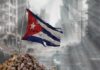 Tattered Cuban flag waving over a pile of rubble in a devastated urban landscape