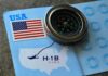 A compass placed on a travel document featuring an H-1B visa and a map of the USA