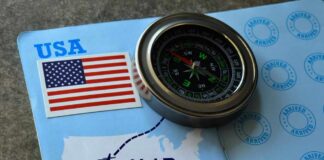 A compass placed on a travel document featuring an H-1B visa and a map of the USA