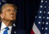 A political figure looking upward beside an American flag