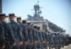 Uniformed naval personnel marching towards a ship