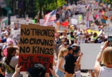 Large crowd at a protest holding signs with various messages