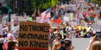 Large crowd at a protest holding signs with various messages
