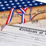 A rolled Declaration of Independence tied with red, white, and blue ribbons next to a birth certificate