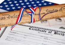 A rolled Declaration of Independence tied with red, white, and blue ribbons next to a birth certificate