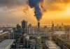 An industrial oil refinery with smoke billowing from a stack at sunset