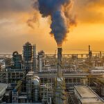 An industrial oil refinery with smoke billowing from a stack at sunset