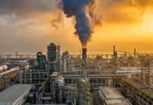 An industrial oil refinery with smoke billowing from a stack at sunset