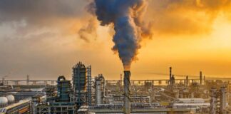 An industrial oil refinery with smoke billowing from a stack at sunset