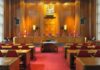 Interior view of a courtroom with wooden paneling and red seating