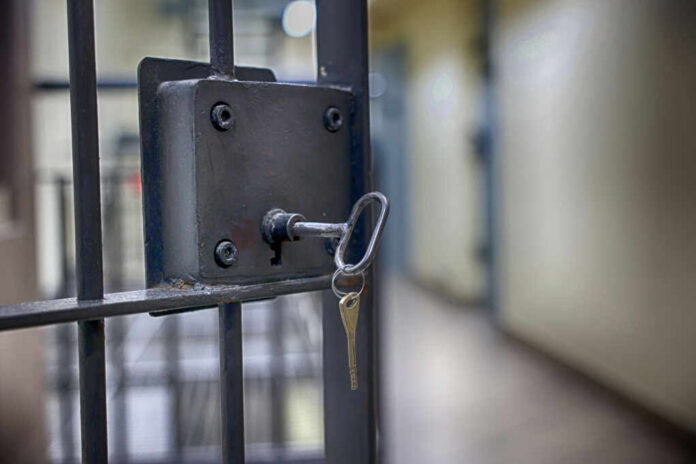 Close-up of a locked jail cell door with a key inserted