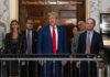 A group of individuals, including a political figure, standing in front of a courtroom entrance