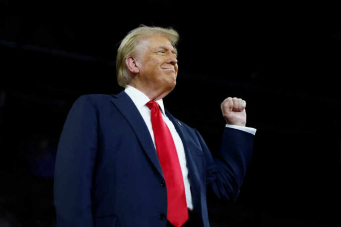 shutterstock2540189359-1jpg A man in a suit with a red tie raising his fist confidently during a speech