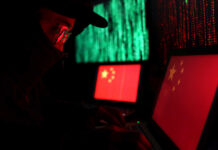 A person in a dark setting working on laptops displaying the Chinese flag