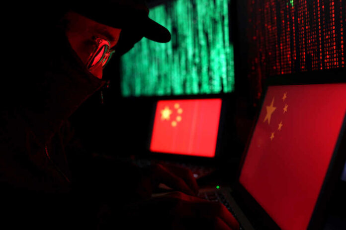 A person in a dark setting working on laptops displaying the Chinese flag