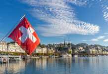 EU Fears: Swiss Population Vote Hits Nerve Swiss flag waving in front of Lake Lucerne with a city skyline in the background