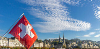 EU Fears: Swiss Population Vote Hits Nerve Swiss flag waving in front of Lake Lucerne with a city skyline in the background
