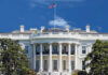 The White House with an American flag flying against a blue sky