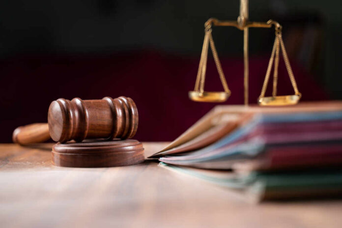 Focus,On,Hammer,,Group,Of,Files,On,Judge,Table,Covered A wooden gavel and scales of justice on a table with law books