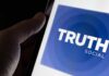 Close-up of a hand holding a smartphone displaying the Truth Social app logo