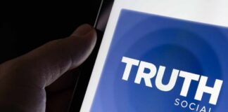 Close-up of a hand holding a smartphone displaying the Truth Social app logo