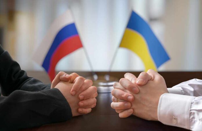 Clasped hands of two individuals with Russian and Ukrainian flags in the background