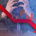 A stressed businessman holding his head with a downward stock market graph in the background