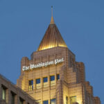 The top of a building featuring the sign of The Washington Post against a blue evening sky