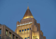 Washington Post SLASHED: 30% Staff AXED The top of a building featuring the sign of The Washington Post against a blue evening sky
