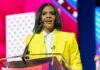 A woman in a bright yellow suit speaking at a podium during a conference