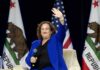 Woman in blue suit waving while seated with microphone