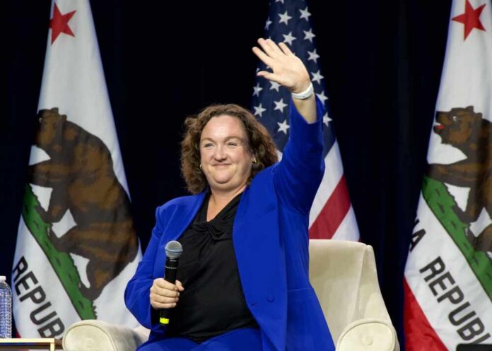 Woman in blue suit waving while seated with microphone