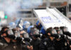 Riot police in gas masks with shields amid smoke