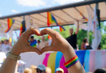 Hands forming a heart shape in front of a Pride celebration stage