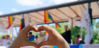 Hands forming a heart shape in front of a Pride celebration stage