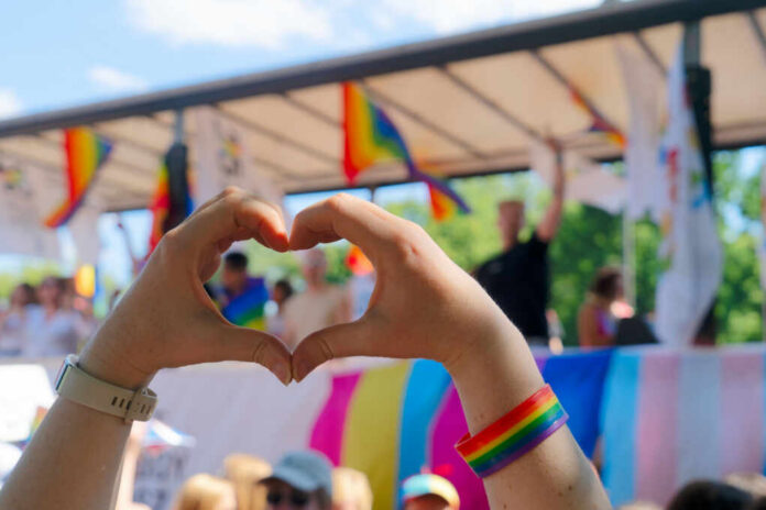 shutterstock_2464411259 Hands forming a heart shape in front of a Pride celebration stage